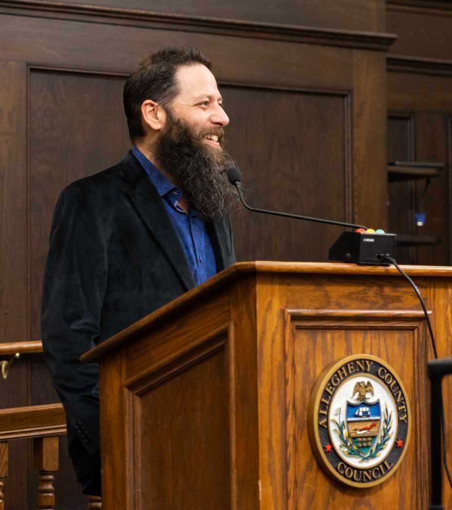 John Schalcosky speaking at a podium in Allegheny County Council chambers.